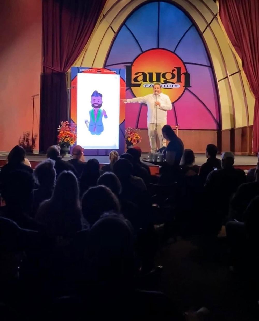 A comic on the Laugh Factory Las Vegas stage beside a VR comic in the Proto hologram box